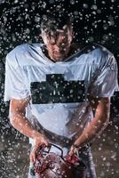 American Football Field Lonely Athlete Warrior Standing on a Field Holds his Helmet and Ready to Play. Player Preparing to Run, Attack and Score Touchdown. Rainy Night with Dramatic Fog, Blue Light photo