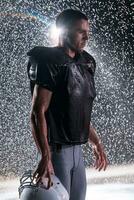 American Football Field Lonely Athlete Warrior Standing on a Field Holds his Helmet and Ready to Play. Player Preparing to Run, Attack and Score Touchdown. Rainy Night with Dramatic Fog, Blue Light photo