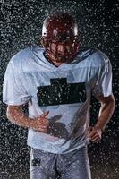 American Football Field Lonely Athlete Warrior Standing on a Field Holds his Helmet and Ready to Play. Player Preparing to Run, Attack and Score Touchdown. Rainy Night with Dramatic Fog, Blue Light photo