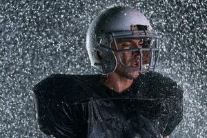 American Football Field Lonely Athlete Warrior Standing on a Field Holds his Helmet and Ready to Play. Player Preparing to Run, Attack and Score Touchdown. Rainy Night with Dramatic Fog, Blue Light photo