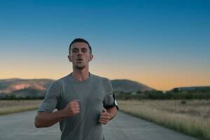 Attractive fit man running fast along countryside road at sunset light, doing jogging workout outdoors photo