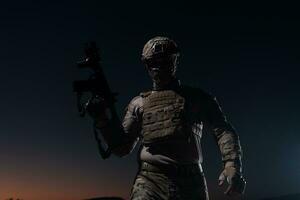 Army soldier in Combat Uniforms with an assault rifle, plate carrier and combat helmet going on a dangerous mission on a rainy night. photo