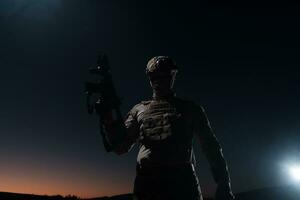 Army soldier in Combat Uniforms with an assault rifle, plate carrier and combat helmet going on a dangerous mission on a rainy night. photo