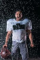 American Football Field Lonely Athlete Warrior Standing on a Field Holds his Helmet and Ready to Play. Player Preparing to Run, Attack and Score Touchdown. Rainy Night with Dramatic Fog, Blue Light photo