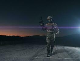 Army soldier in Combat Uniforms with an assault rifle, plate carrier and combat helmet going on a dangerous mission on a rainy night. photo