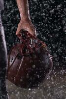 Close up of American Football Athlete Warrior Standing on a Field focus on his Helmet and Ready to Play. Player Preparing to Run, Attack and Score Touchdown. Rainy Night with Dramatic lens flare and rain drops. photo