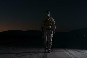 Ejército soldado en combate uniformes con un asalto rifle, plato portador y combate casco yendo en un peligroso misión en un lluvioso noche. foto