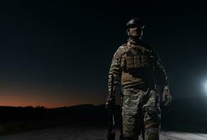 Army soldier in Combat Uniforms with an assault rifle, plate carrier and combat helmet going on a dangerous mission on a rainy night. photo