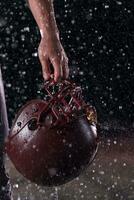 Close up of American Football Athlete Warrior Standing on a Field focus on his Helmet and Ready to Play. Player Preparing to Run, Attack and Score Touchdown. Rainy Night with Dramatic lens flare and rain drops. photo