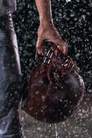 Close up of American Football Athlete Warrior Standing on a Field focus on his Helmet and Ready to Play. Player Preparing to Run, Attack and Score Touchdown. Rainy Night with Dramatic lens flare and rain drops. photo