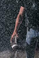 americano fútbol americano campo solitario atleta guerrero en pie en un campo sostiene su casco y Listo a jugar. jugador preparando a correr, ataque y Puntuación aterrizaje. lluvioso noche con dramático niebla, azul ligero foto