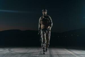 Army soldier in Combat Uniforms with an assault rifle, plate carrier and combat helmet going on a dangerous mission on a rainy night. photo