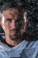 American Football Field Lonely Athlete Warrior Standing on a Field Holds his Helmet and Ready to Play. Player Preparing to Run, Attack and Score Touchdown. Rainy Night with Dramatic Fog, Blue Light photo