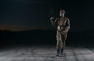 Ejército soldado en combate uniformes con un asalto rifle, plato portador y combate casco yendo en un peligroso misión en un lluvioso noche. foto