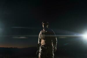 Ejército soldado en combate uniformes con un asalto rifle, plato portador y combate casco yendo en un peligroso misión en un lluvioso noche. foto