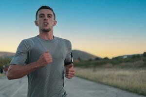 Attractive fit man running fast along countryside road at sunset light, doing jogging workout outdoors photo