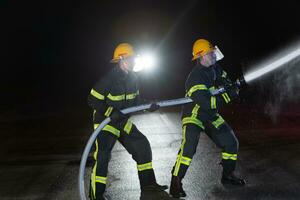 Firefighters use a water hose to eliminate a fire hazard. Team of firemen in the dangerous rescue mission. photo