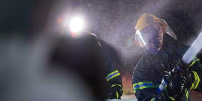 bomberos utilizando un agua manguera a eliminar un fuego peligro. equipo de hembra y masculino bomberos en peligroso rescate misión. foto