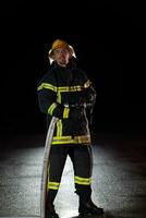 bombero en fuego luchando operación. retrato de un heroico bombero en un protector traje y rojo casco en acción durante pesado lluvia. foto