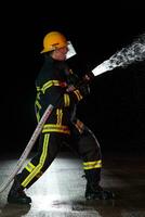 bombero en fuego luchando operación. retrato de un heroico bombero en un protector traje y rojo casco en acción durante pesado lluvia. foto