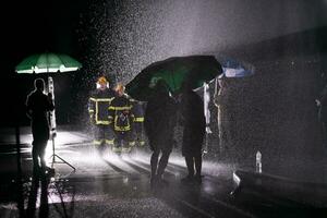 Behind the scene of Firefighters photo and cinema set with rain use a water hose to eliminate a fire hazard.