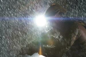 Army soldier in Combat Uniforms with an assault rifle, plate carrier and combat helmet going on a dangerous mission on a rainy night. photo