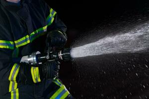 bomberos utilizar un agua manguera a eliminar un fuego peligro. equipo de bomberos en el peligroso rescate misión. foto