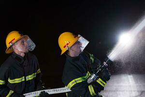 bomberos utilizar un agua manguera a eliminar un fuego peligro. equipo de bomberos en el peligroso rescate misión. foto