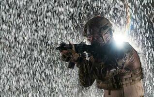 Ejército soldado en combate uniformes con un asalto rifle, plato portador y combate casco yendo en un peligroso misión en un lluvioso noche. foto