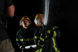 bomberos utilizar un agua manguera a eliminar un fuego peligro. equipo de bomberos en el peligroso rescate misión. foto