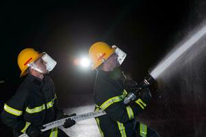 Firefighters use a water hose to eliminate a fire hazard. Team of firemen in the dangerous rescue mission. photo