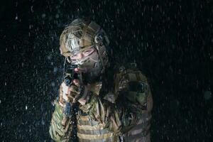 Army soldier in Combat Uniforms with an assault rifle, plate carrier and combat helmet going on a dangerous mission on a rainy night. photo