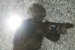 Army soldier in Combat Uniforms with an assault rifle, plate carrier and combat helmet going on a dangerous mission on a rainy night. photo