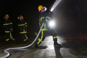 bomberos utilizar un agua manguera a eliminar un fuego peligro. equipo de bomberos en el peligroso rescate misión. foto