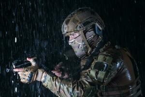 Army soldier in Combat Uniforms with an assault rifle, plate carrier and combat helmet going on a dangerous mission on a rainy night. photo