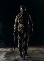 Army soldier in Combat Uniforms with an assault rifle, plate carrier and combat helmet going on a dangerous mission on a rainy night. photo