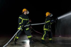 bomberos utilizando un agua manguera a eliminar un fuego peligro. equipo de hembra y masculino bomberos en peligroso rescate misión. foto