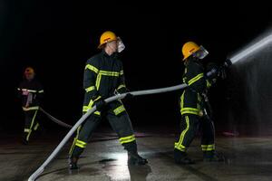 bomberos utilizando un agua manguera a eliminar un fuego peligro. equipo de hembra y masculino bomberos en peligroso rescate misión. foto