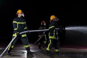 bomberos utilizando un agua manguera a eliminar un fuego peligro. equipo de hembra y masculino bomberos en peligroso rescate misión. foto