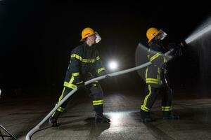 Firefighters using a water hose to eliminate a fire hazard. Team of female and male firemen in dangerous rescue mission. photo