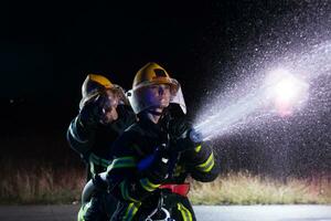 bomberos utilizando un agua manguera a eliminar un fuego peligro. equipo de hembra y masculino bomberos en peligroso rescate misión. foto