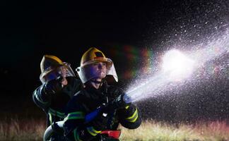 bomberos utilizando un agua manguera a eliminar un fuego peligro. equipo de hembra y masculino bomberos en peligroso rescate misión. foto