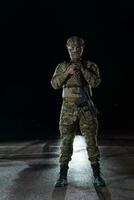 Army soldier in Combat Uniforms with an assault rifle, plate carrier and combat helmet going on a dangerous mission on a rainy night. photo