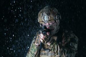 Ejército soldado en combate uniformes con un asalto rifle, plato portador y combate casco yendo en un peligroso misión en un lluvioso noche. foto