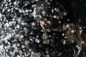 Army soldier in Combat Uniforms with an assault rifle, plate carrier and combat helmet going on a dangerous mission on a rainy night. photo