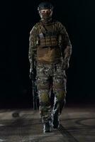 Army soldier in Combat Uniforms with an assault rifle, plate carrier and combat helmet going on a dangerous mission on a rainy night. photo
