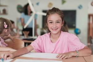 Little girls sitting in elementary school drawing on paper with their friends while sitting in a modern classroom photo