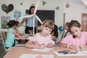 Little girls sitting in elementary school drawing on paper with their friends while sitting in a modern classroom photo