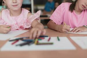 Little girls sitting in elementary school drawing on paper with their friends while sitting in a modern classroom photo