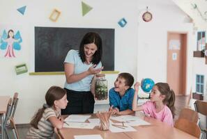 Female Teacher with kids in biology class at elementary school conducting biology or botanical scientific experiment about sustainable Growing plants. Learning about plants in a glass jar photo